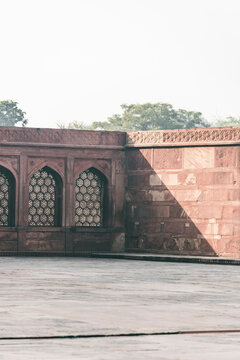 View of the intricate and beautiful tomb of Akbar with red sandstone arches surrounded by trees, Agra, India.
