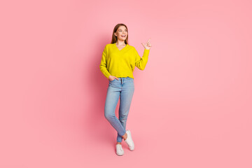 Young woman in casual outfit pointing sideways on pink background for advertisement