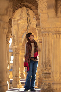 View of ornate columns and an arch with a traditional woman in a historical site, Bada Bagh, Jaisalmer, India.