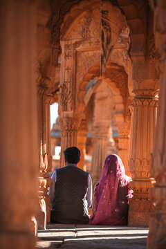 View of ornate sandstone arches and columns with a couple sitting in traditional clothing, Bada Bagh, Jaisalmer, India.