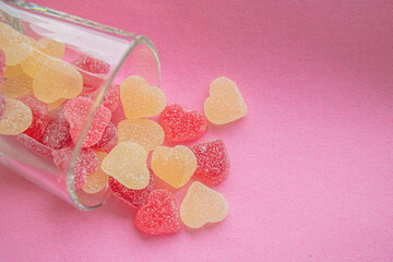 Colorful gummy hearts pouring out of glass on pink background, top view, valentines day concept