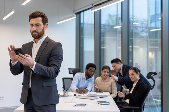 Team criticizing and discussing behind male colleague boss back, diverse business team at work place inside office.