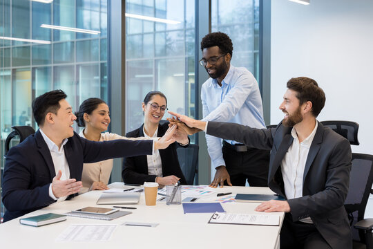 Successful diverse business team joyfully putting hands together, giving high five. Team of financiers investors in business suits celebrating successful achievement results at workplace.