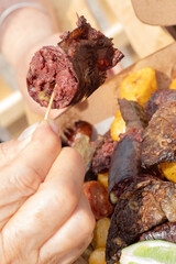 Close-up of a portion of blood sausage lifted with a toothpick by a person's hand. Fritanga,...
