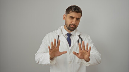 Hispanic man in white coat making calm gesture on white isolated background, expressing tranquility and confidence, embodying professional assurance and composed demeanor.