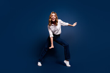 Obraz premium Joyful young woman in stylish outfit dancing against dark blue background, embracing lifestyle and fashion