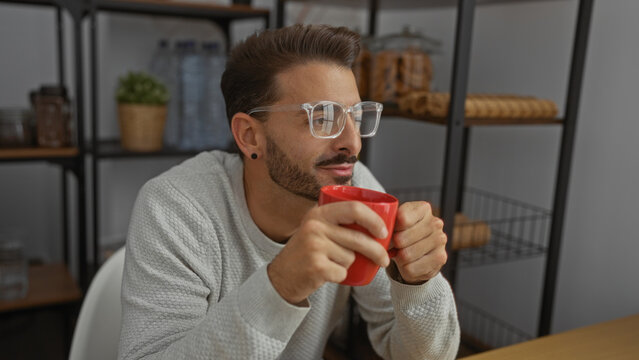 Young man in office drinking coffee holding red mug glasses relaxed indoor portrait attractive handsome casual setting