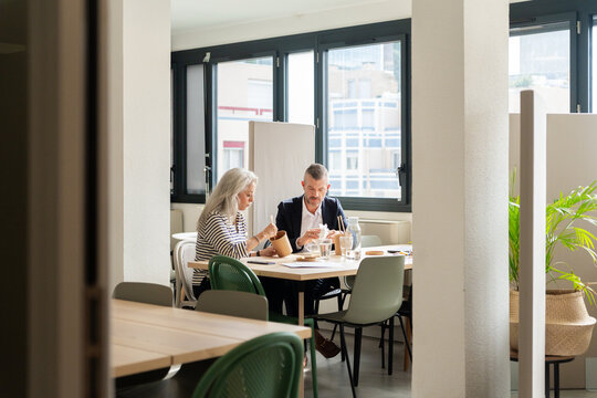 Mature Colleagues Having Lunch Meeting In Bright Office Kitchen.


