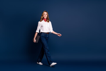 Obraz premium Trendy young woman in casual attire walking confidently against dark blue background