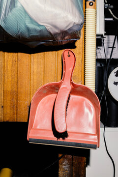 Red hand brush and dust pan hanging on wood panel wall