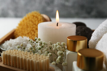 Burning candle and other spa supplies on table, closeup