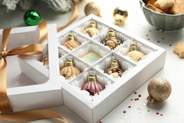 Box with tasty chocolate candies in shape of baubles and Christmas decor on white background, closeup