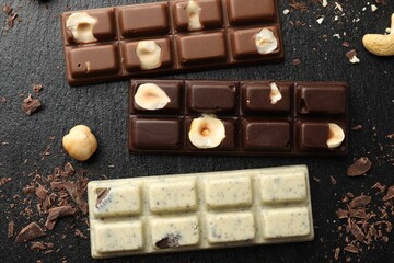 Different tasty chocolate bars with nuts on black table, flat lay