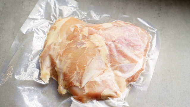 Vacuum-sealed raw chicken breast in plastic packaging on a grey countertop, showcasing fresh poultry meat ready for cooking or storage with a focus on freshness and food preservation