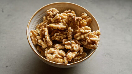 Closeup of a bowl filled with fresh walnuts on a grey surface.