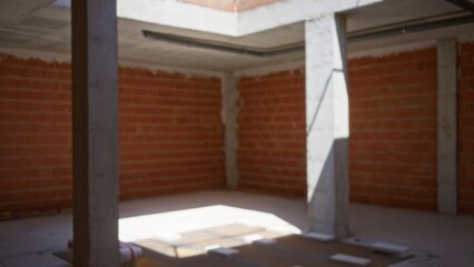 Defocused view of an unfinished construction site with brick walls and concrete pillars, illuminated by natural light filtering through an unfurnished ceiling, creating a blurred, bokeh effect.
