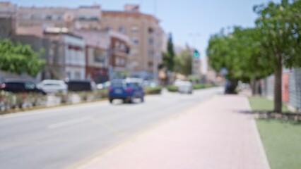Blurred outdoor scene showing a defocused street with buildings, cars, trees, and people in the background, capturing a typical urban day
