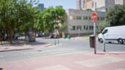 Blurred urban outdoor scene with defocused trees, buildings, crosswalk, van, stop sign, and pedestrian area on a sunny day