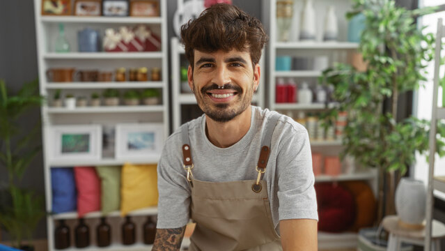 Young hispanic man with beard smiling in a home decor store interior with colorful decorations and plants