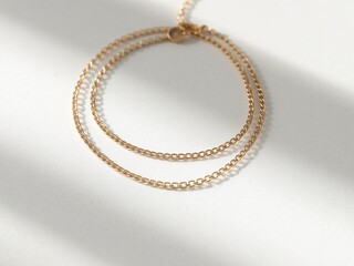 A minimalist gold chain necklace neatly coiled on a matte white stone background, illuminated with diffused natural light
