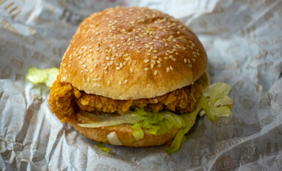 Delicious chicken burger with sesame seed bun and fresh lettuce on a crumpled paper background.