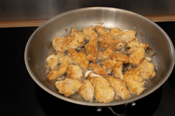 Metal frying pan on glass stove. Chicken pieces are fried in the pan. Home cooking