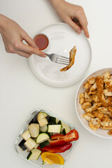 Female hand holding fork with piece of chicken. Homemade food on white table. Top view, copy space