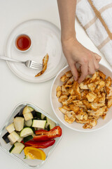 Female hands take a piece of fried chicken. Vegetables and plate on a white table. Top view, copy space