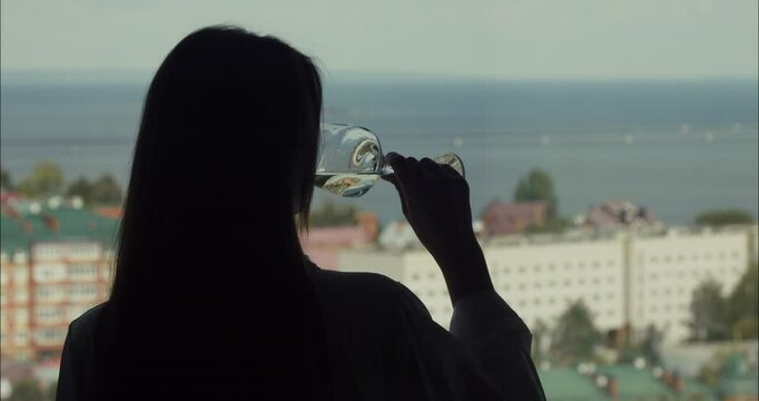 Silhouette of elegant woman sipping wine, enjoying ocean view from hotel