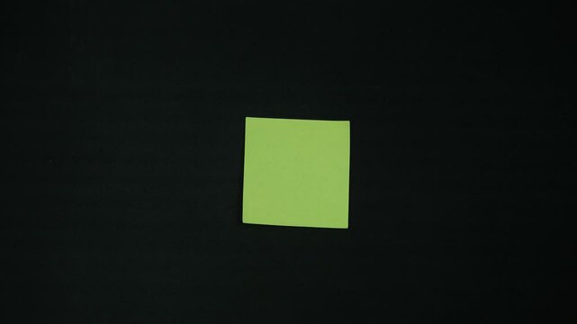 A fragile woman's hand sticks a yellow paper note on black background