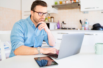 Man working from home typing on computer seated in the kitchen