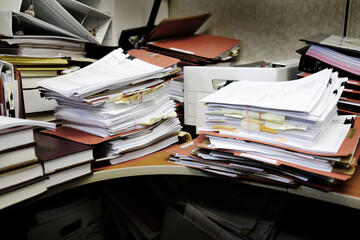 Messy Desk with Books Binders Files and Papers Stacked up High in a Disorganized Office Space
