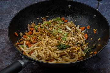 Vegan stir fry in cast iron wok consisting of mixed vegetables,  mung bean sprouts, seitan along...