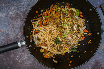 Vegan stir fry in cast iron wok consisting of mixed vegetables,  mung bean sprouts, seitan along with udon noodles