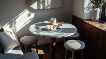 Small breakfast nook with a round marble table, sleek stools, and sunlight highlighting modern decor