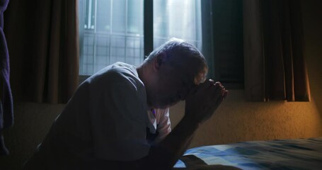 Elderly man sitting on bed with hands clasped in prayer seeking divine guidance and support reflective moment of faith hope and introspection in solitude
