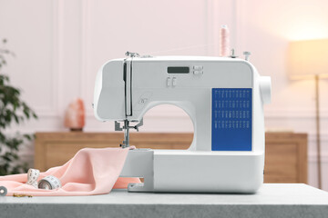 Sewing machine with threads, measuring tape and fabric on white table in workshop