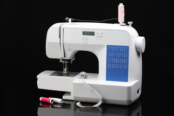 Sewing machine with measuring tape and spools of threads on black background