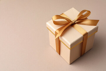Gift box with golden bow on beige background, closeup. Space for text