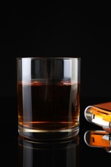 Hip flask and glass of whiskey on black mirror surface, closeup