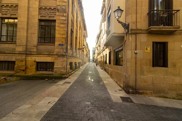 Narrow alley with traditional buildings, balconies, and street lamps in the old town of San Sebastian, Spain. Urban architecture.