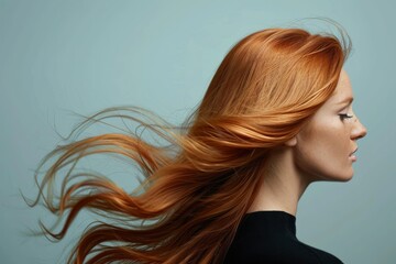 Fototapeta premium A woman with flowing red hair poses gracefully against a soft blue background showcasing beauty and elegance in motion