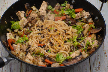 Mushroom, tofu, daikon and carrot stirfry along with udon noodles, cast iron wok, wooden table