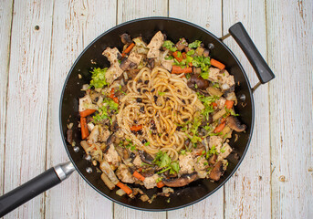 Mushroom, tofu, daikon and carrot stirfry along with udon noodles, cast iron wok, wooden table