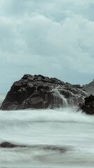 Ocean waves cascading over a rock formation under a cloudy sky