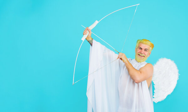 Valentines Day celebration. February 14. Smiling bearded man in angel wings shooting arrow of love from bow. God of love. Valentine day cupid angel with with bow and arrow. Copy space for advertising.