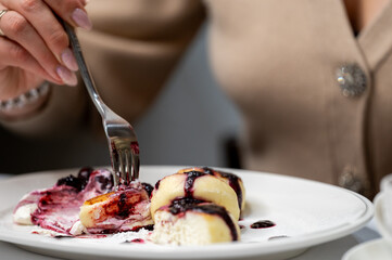 A close-up of a person enjoying a dessert featuring soft dumplings with berry sauce and cream. The fork is poised to take a bite, highlighting the delicious details of the dish.