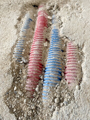 Electrical conduits in construction debris. Close-up of red and blue corrugated electrical conduits partially embedded in concrete with surrounding construction debris.