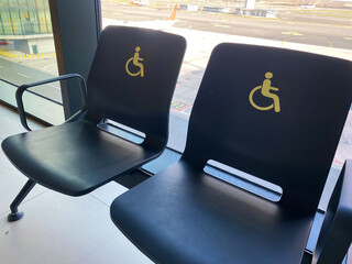 Black chairs with yellow wheelchair symbols designated for disabled passengers at an airport,...