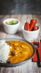Close up photo of a chicken curry dish with rice on a wooden table. Side salad and chillies in the background.